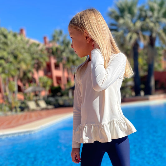 Young girl in a white shirt standing by a pool in Marbella with palm trees in the background
